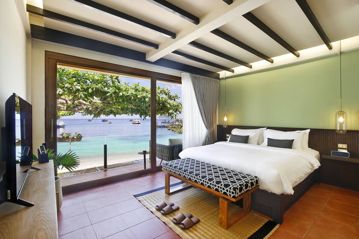 Een hotelkamer met een groot bed, een bankje, een televisie en uitzicht op de oceaan.