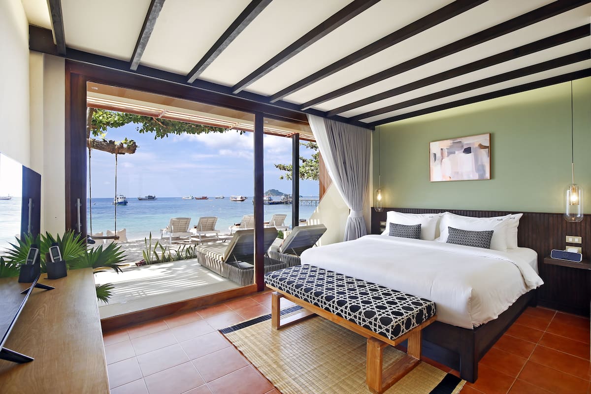 Een hotelkamer met een bed, een bankje, een bureau en uitzicht op de zee.
