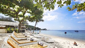 A beachside lounge area with sun loungers and a thatched-roof structure in the background. - Lücke Boutique Hotel (Koh Tao)
