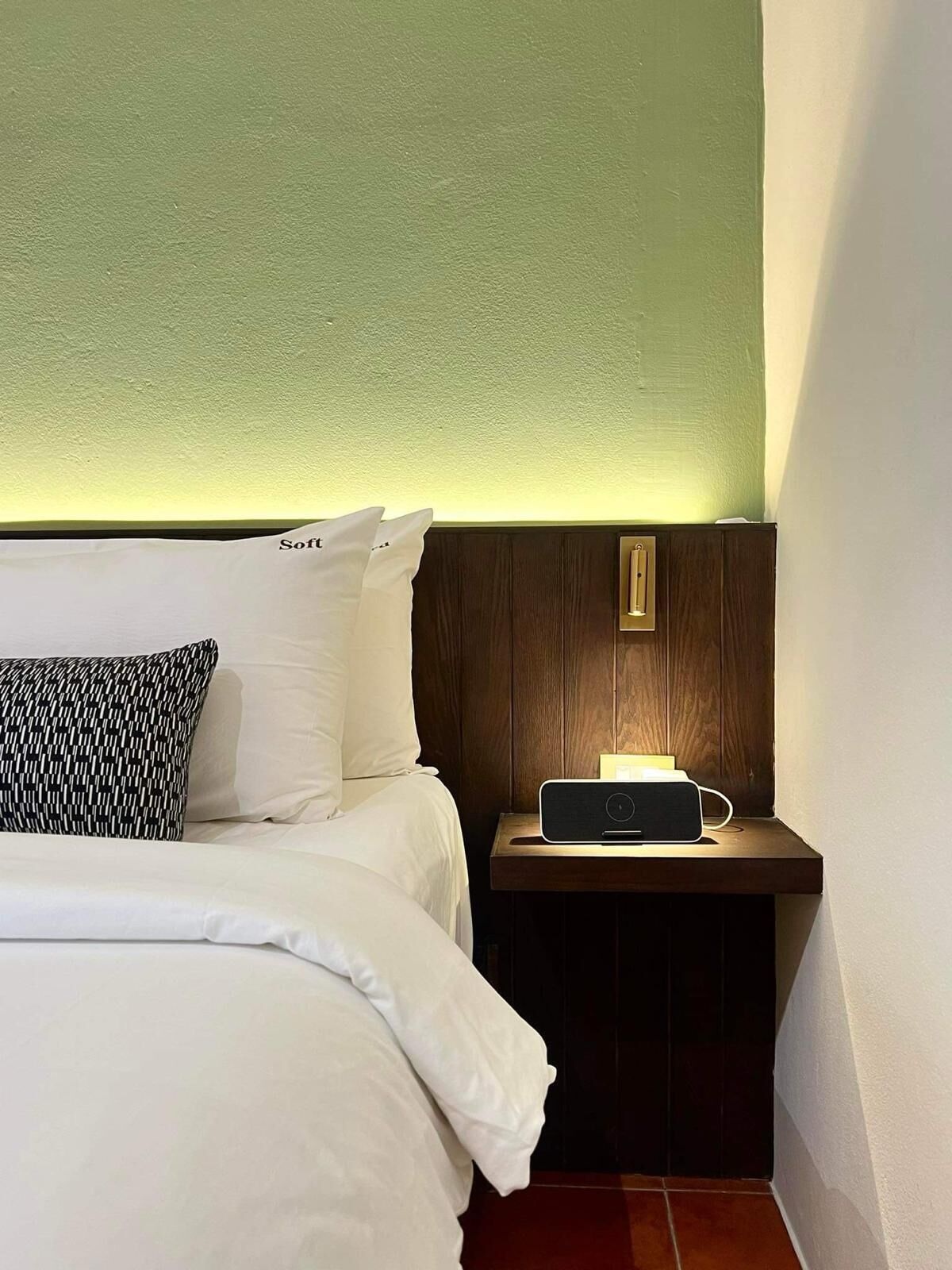 Une chambre d’hôtel avec un lit, une table de chevet avec une lampe et un luminaire fixé au mur.