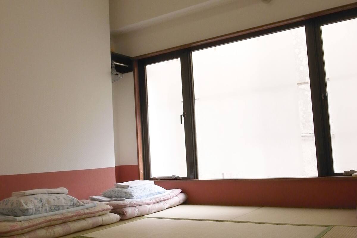 A tatami mat room with a large window, a wall-mounted air conditioner, and a red and white wall trim.