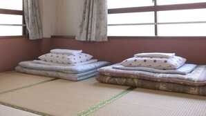 A room with tatami mats, a bed with pillows, a window with curtains, and an air conditioning unit. - Andon Makishikan (Naha)