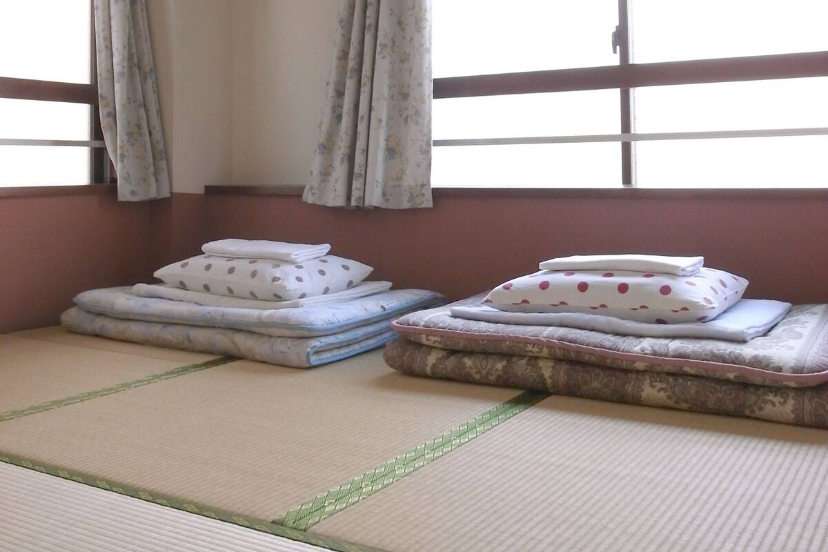 A room with tatami mats, a bed with pillows, a window with curtains, and an air conditioning unit.