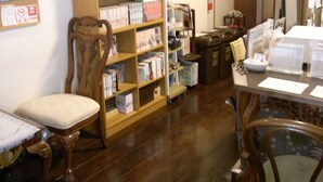 A room with wooden flooring, a bookshelf filled with books, a wooden chair, and a table with papers and a bowl. - Andon Makishikan (Naha)