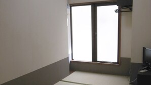 A room with tatami mat flooring, a sliding door, a television on a stand, and an air conditioning unit on the wall. - Andon Makishikan (Naha)