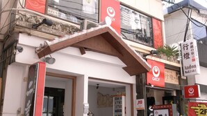 A building with a red and white sign, a small entrance, and a vending machine outside. - Andon Makishikan (Naha)