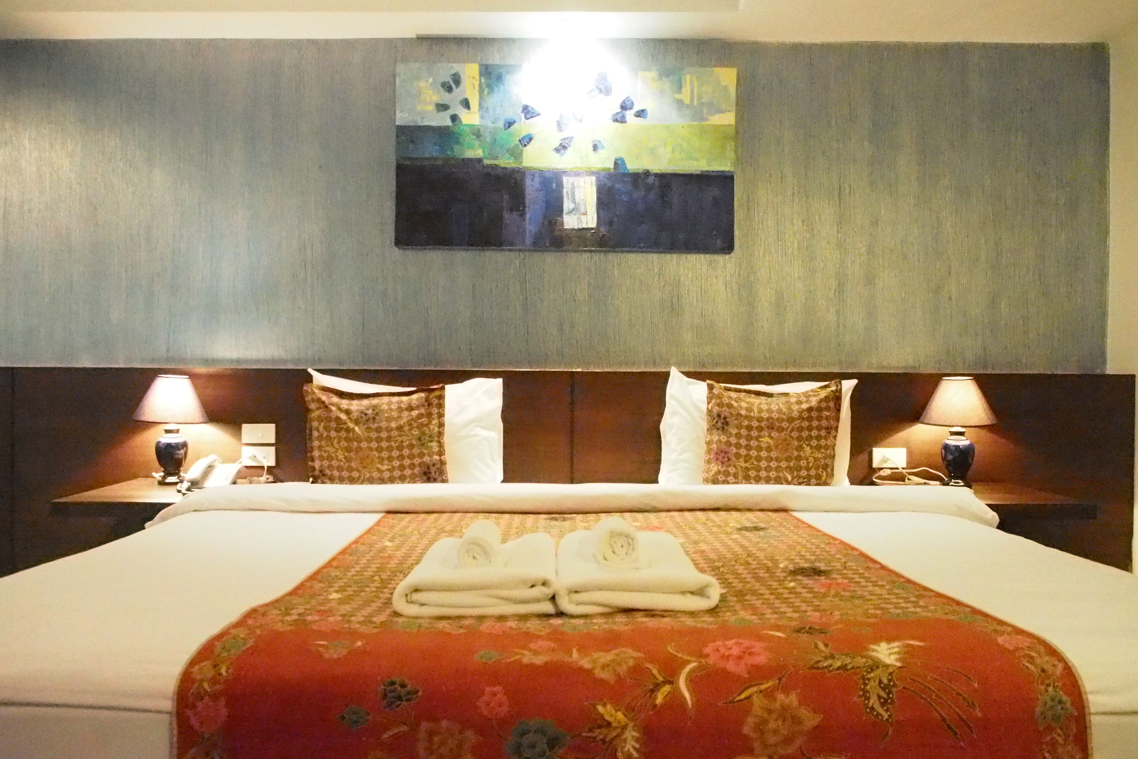 Une chambre d’hôtel avec un grand lit, deux tables de chevet avec des lampes, un tableau au mur et une couvre-lit à motifs floraux.