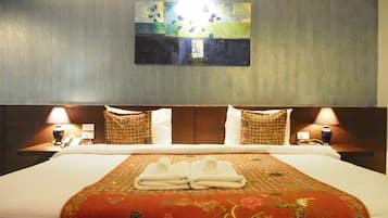 Quarto de hotel com uma cama grande, duas mesas de cabeceira com luminárias, um quadro na parede e um edredom estampado com flores.