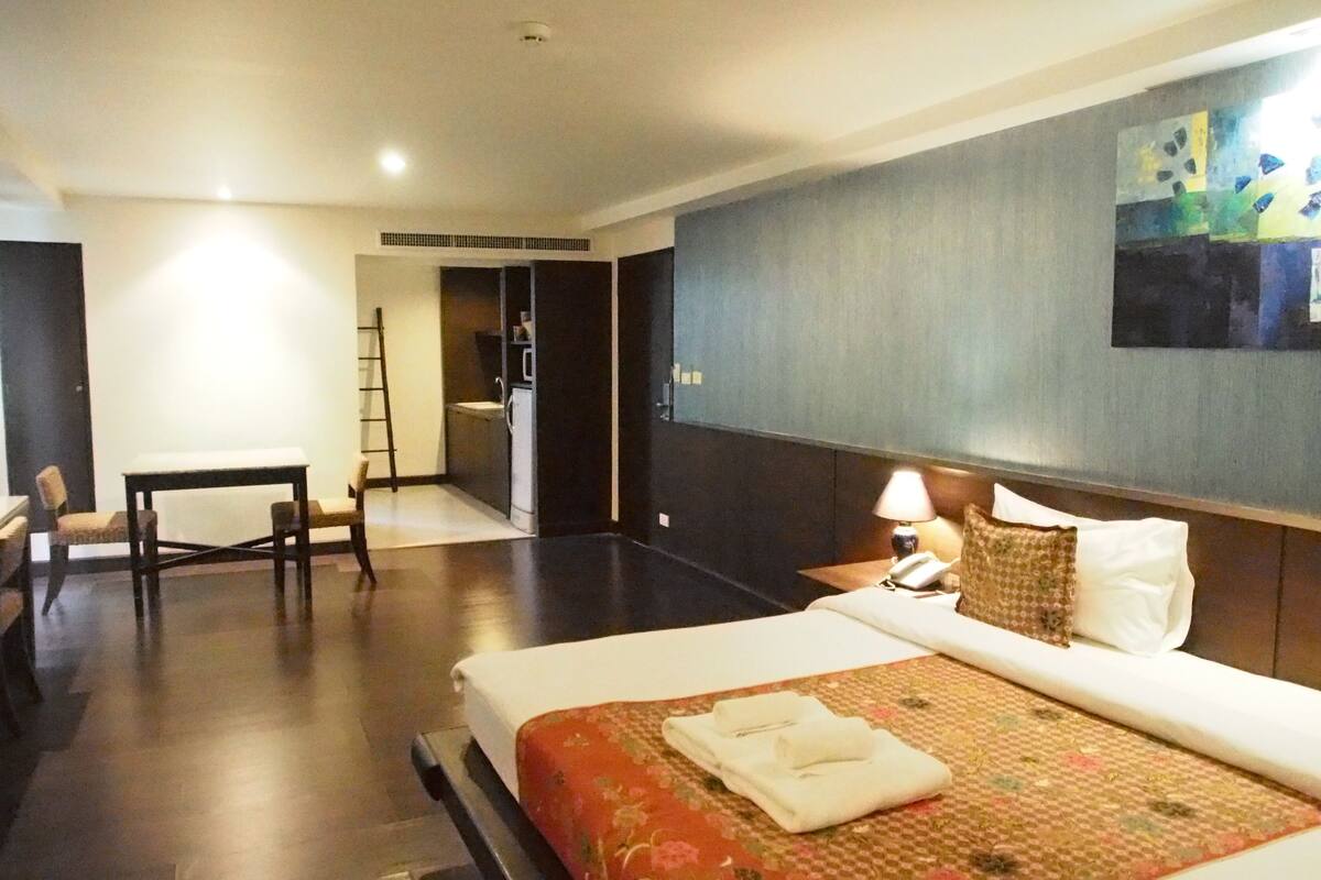 A hotel room with a bed, a desk, a chair, a nightstand, and a painting on the wall.