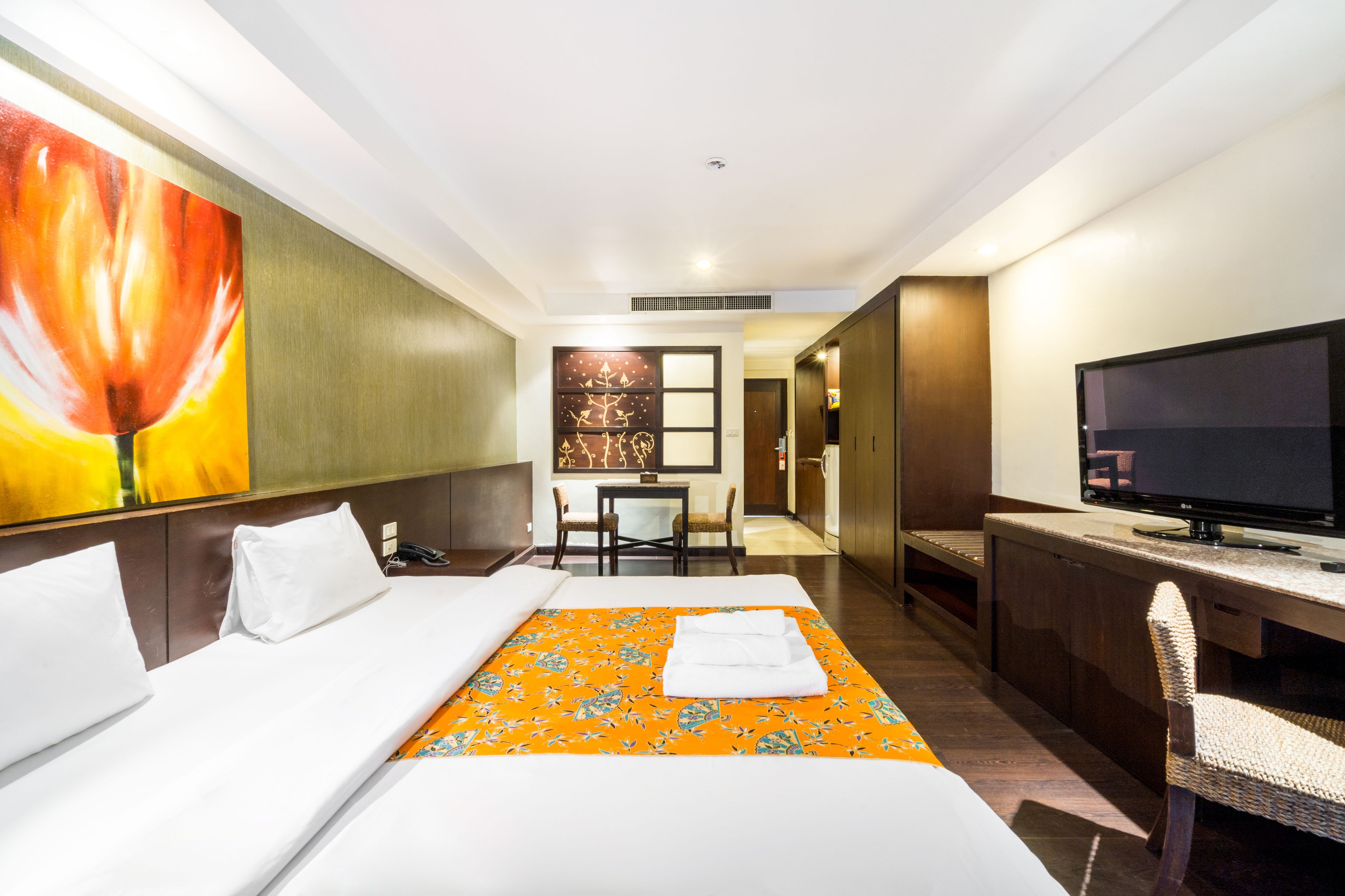 A hotel room with a bed, a desk with a television, a dining area, and a large painting on the wall.