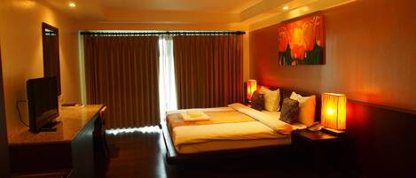 A hotel room with a bed, a TV, a desk, and a painting on the wall.