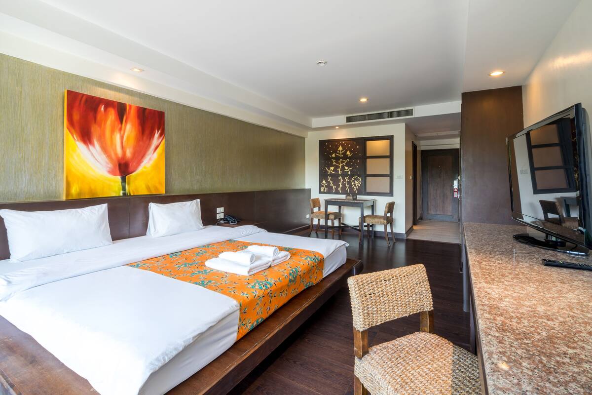 A hotel room with a large bed, a desk, chairs, and a television.