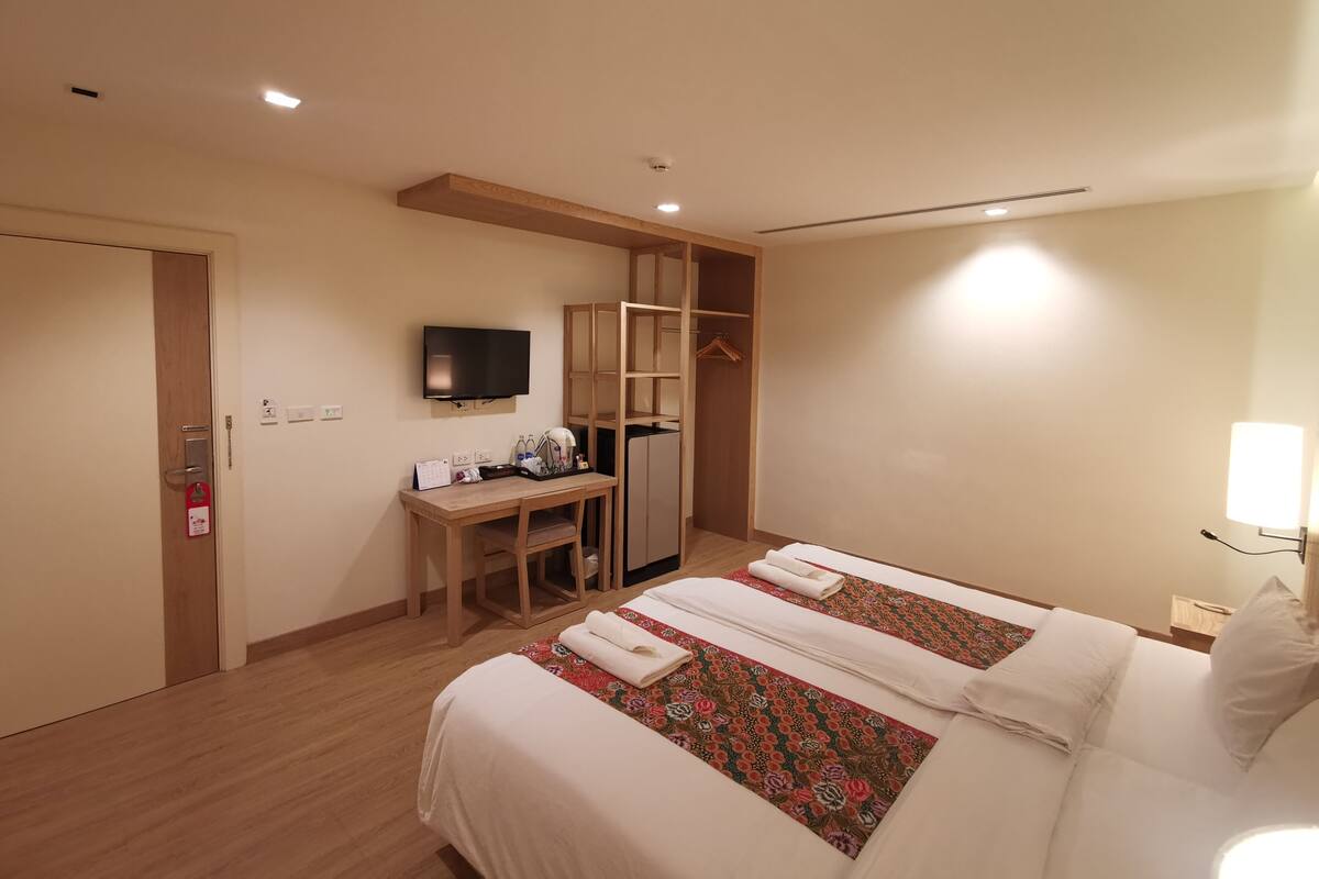 A hotel room with two beds, a desk, a television, and a wardrobe.