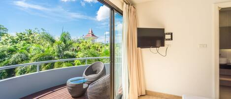 A balcony with wicker chairs, a TV mounted on the wall, and a view of greenery and a gazebo.