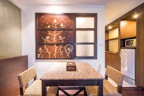 A dining area with a table and chairs, a decorative wall panel, and a kitchen area with a refrigerator. - Baan Suwantawe (Phuket)