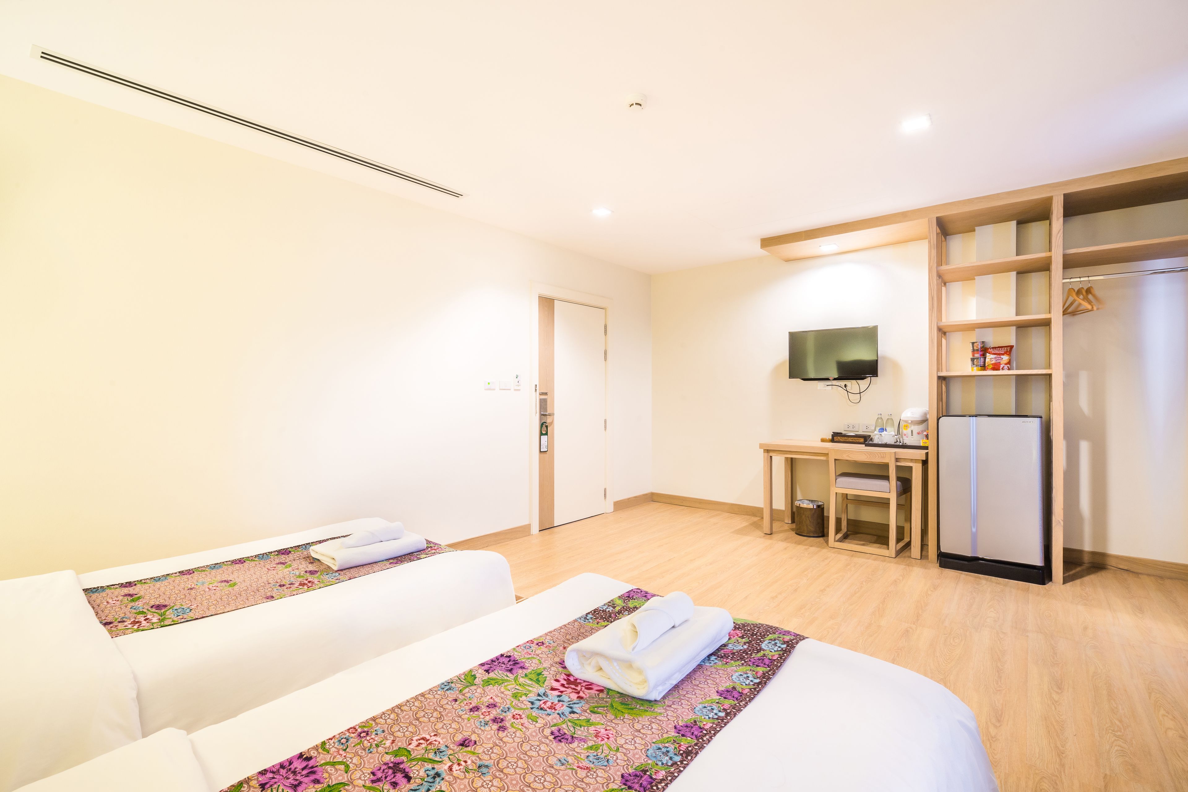 A hotel room with two beds, a desk, a television, and a refrigerator.