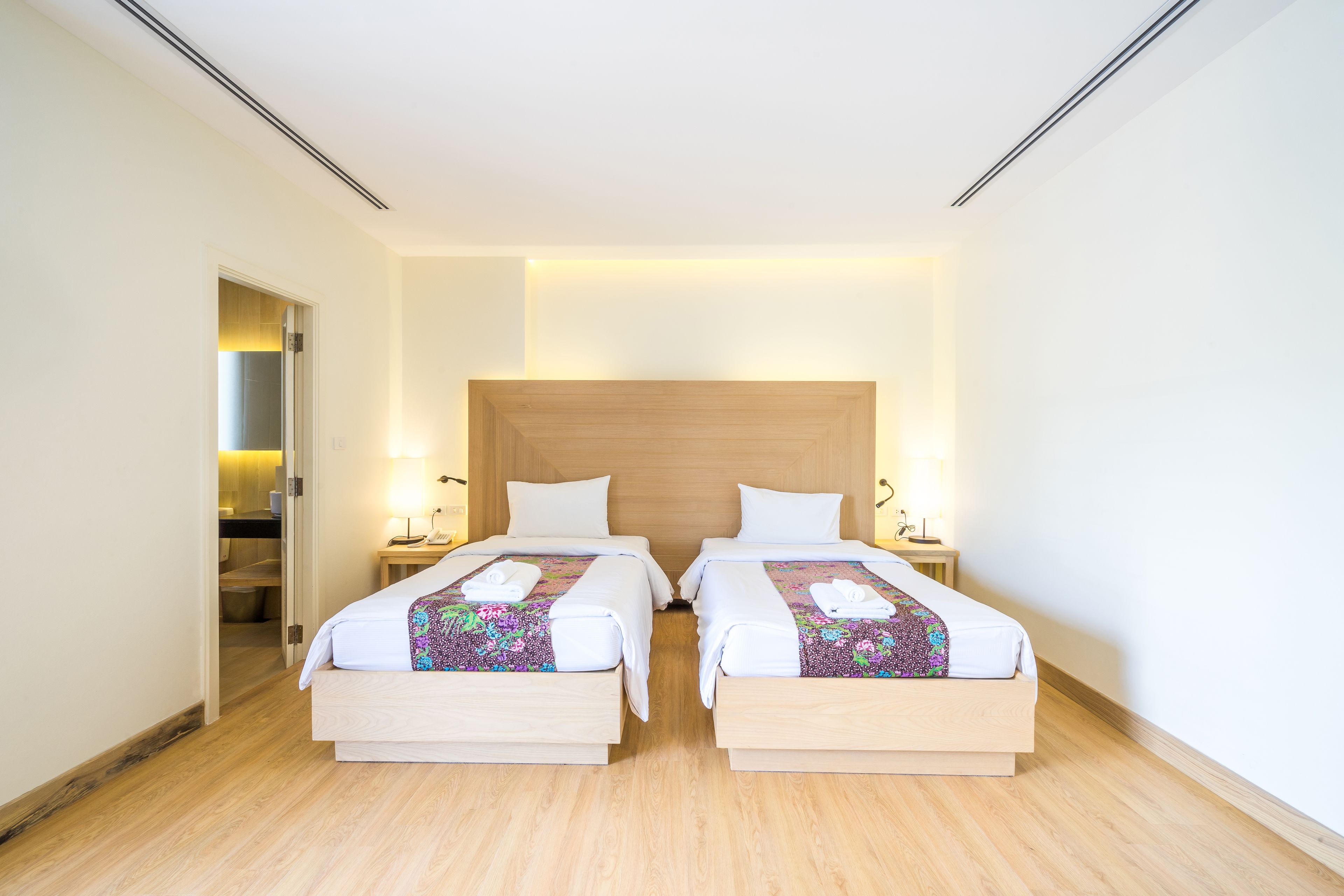 A hotel room with two beds, wooden flooring, and a large wooden headboard.