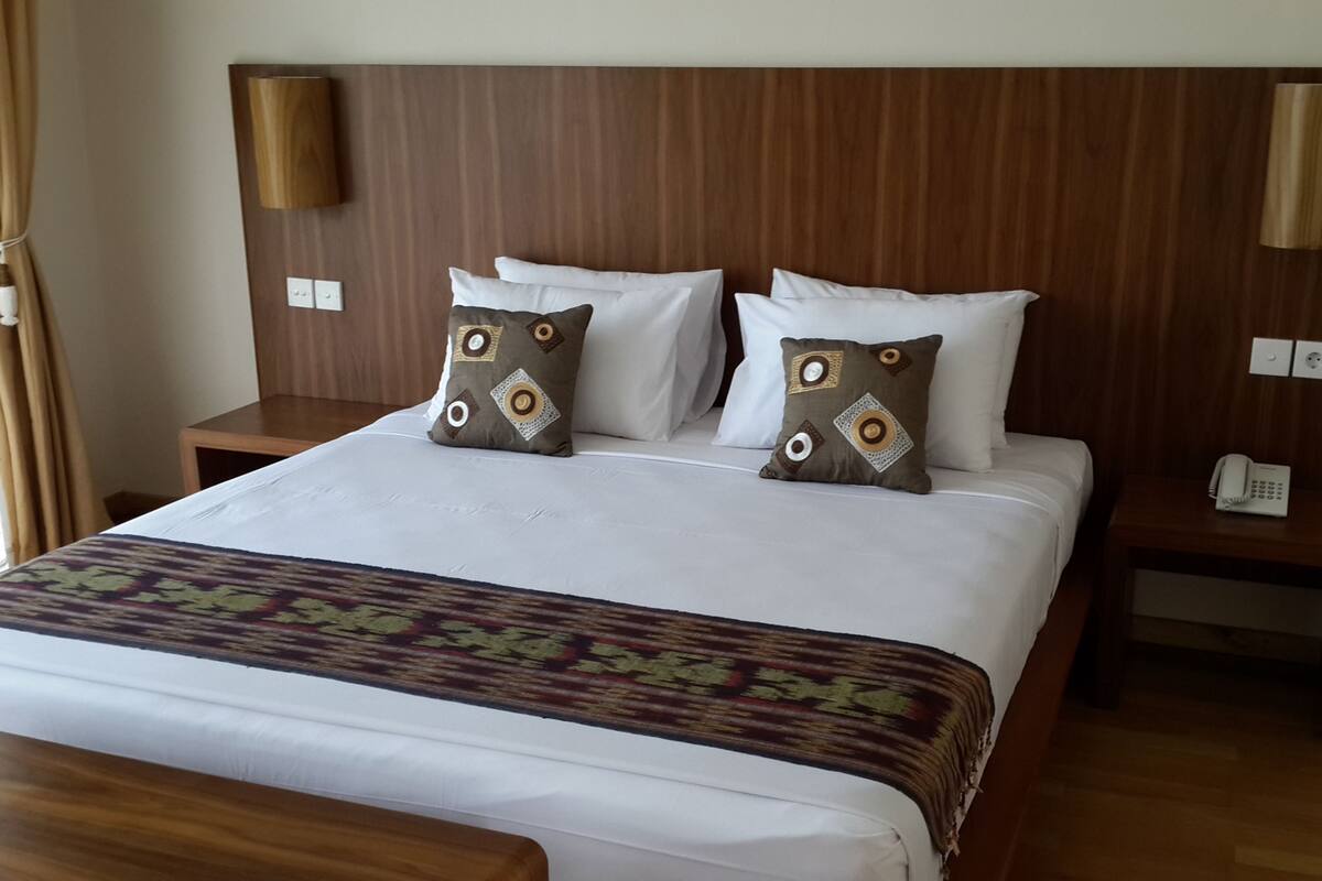 A hotel room with a large bed, two bedside tables, a wooden headboard, and a patterned bedspread.