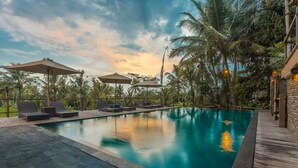 A pool area with lounge chairs and umbrellas, surrounded by palm trees and a wooden deck. - Manyi Village (Ubud)