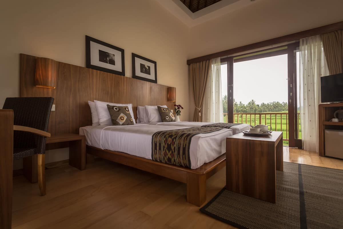 A spacious bedroom with a large bed, wooden headboard, and a view of a lush landscape through the sliding glass door.