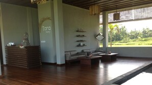 A modern interior with a reception desk, sofas, a coffee table, and a view of a lush garden. - Manyi Village (Ubud)