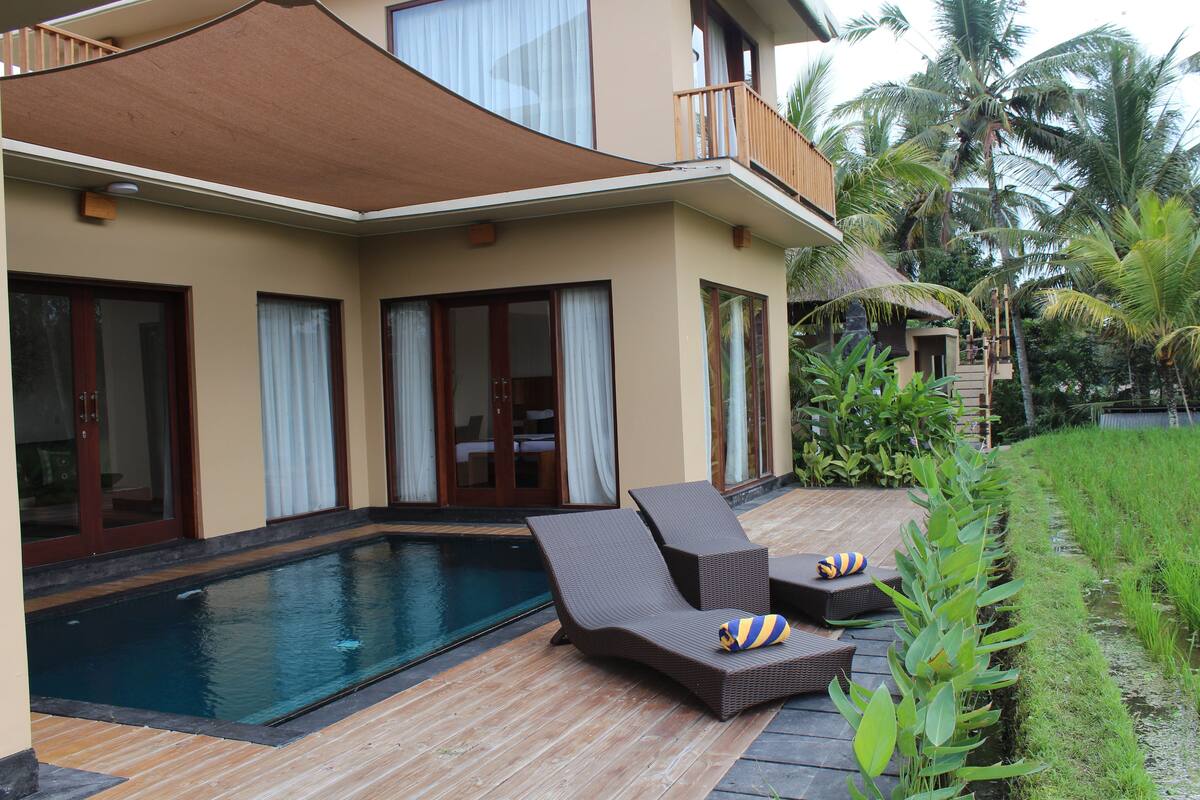 A poolside area with lounge chairs and a pool, surrounded by a house with large windows and a balcony.