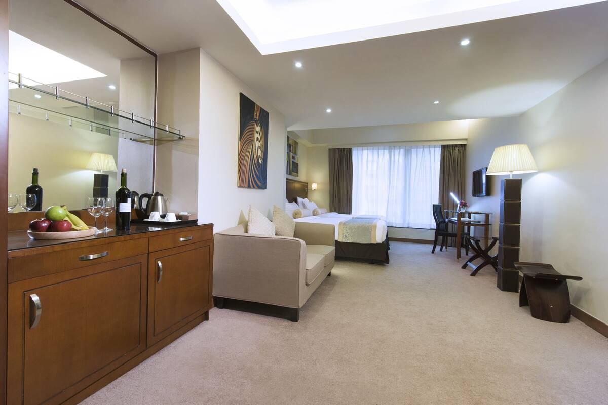 A hotel room with a bed, a sofa, a desk, and a dining area. There is a large mirror, a painting, and a lamp.
