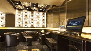 A modern hotel lobby with a black leather sofa, a small round table, and a computer monitor displaying "BRIGHTON HOTEL". - Brighton Hotel Hong Kong (Hong Kong)