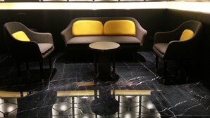 A modern lounge area with a sofa and two armchairs, a small round table, and a geometric patterned wall. - Brighton Hotel Hong Kong (Hong Kong)