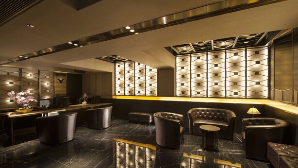 A modern lobby with a reception desk, seating area, and decorative wall panels. - Brighton Hotel Hong Kong (Hong Kong)