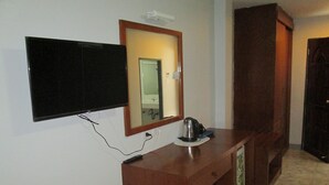 Habitación de hotel con televisor de pantalla plana en la pared, un escritorio de madera con tetera y control remoto, y un espejo sobre el escritorio.