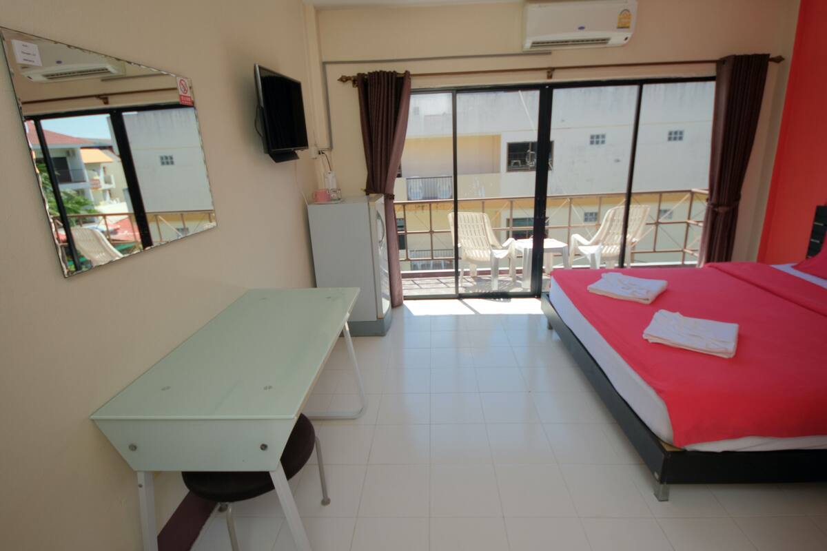 A hotel room with a bed, a desk, a chair, a TV, and a balcony with chairs.