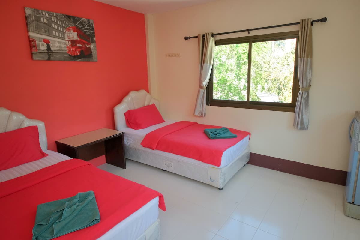 A hotel room with two beds, each with red bedding, a small bedside table, and a window with curtains.