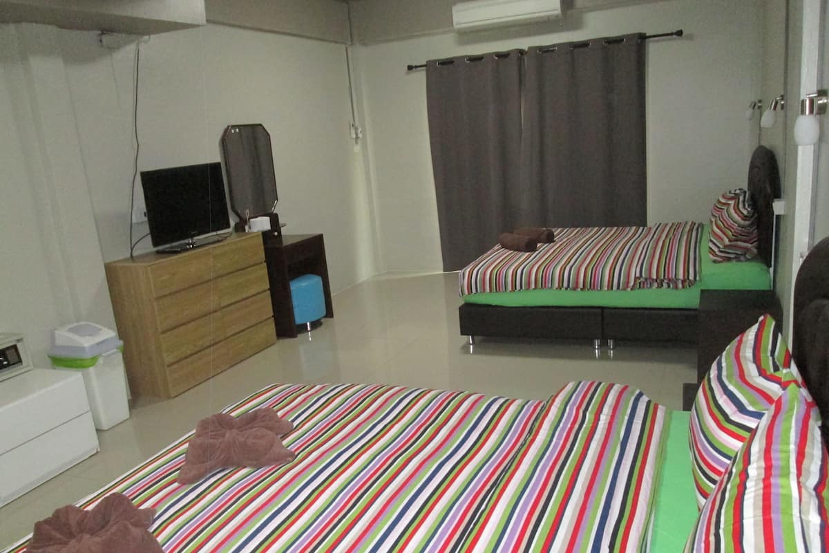 A bedroom with two beds, a wooden dresser, a television, and a small table with a blue object on it.