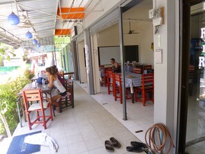 An outdoor cafe with wooden tables and chairs, a tiled floor, and a glass door leading inside. - Pineapple Guesthouse (Karon)