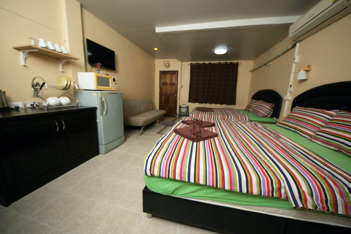 A compact hotel room with a bed, a small kitchenette, a sofa, and a television.