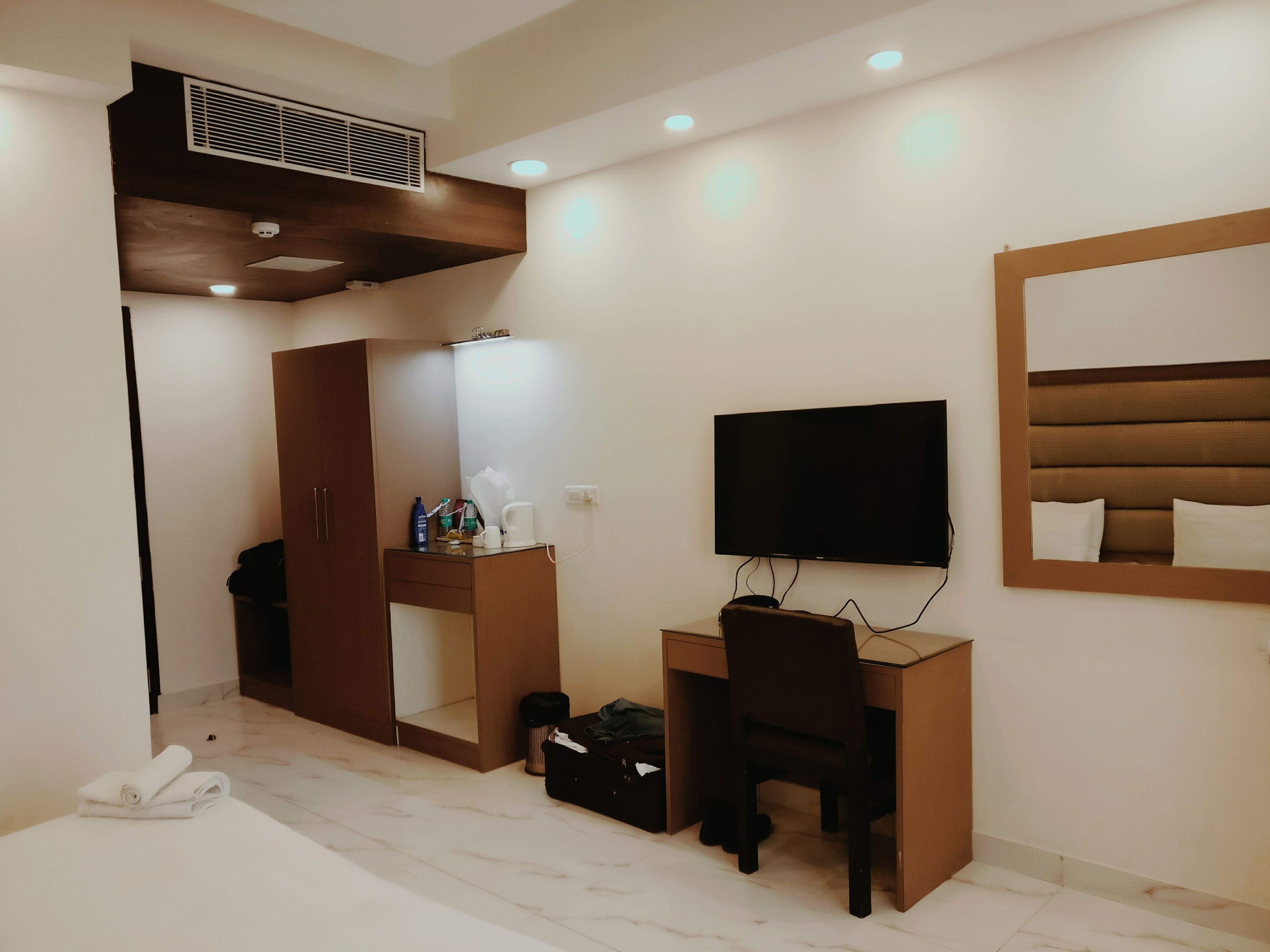 A hotel room with a bed, a desk with a chair, a TV, a wardrobe, and a mirror.
