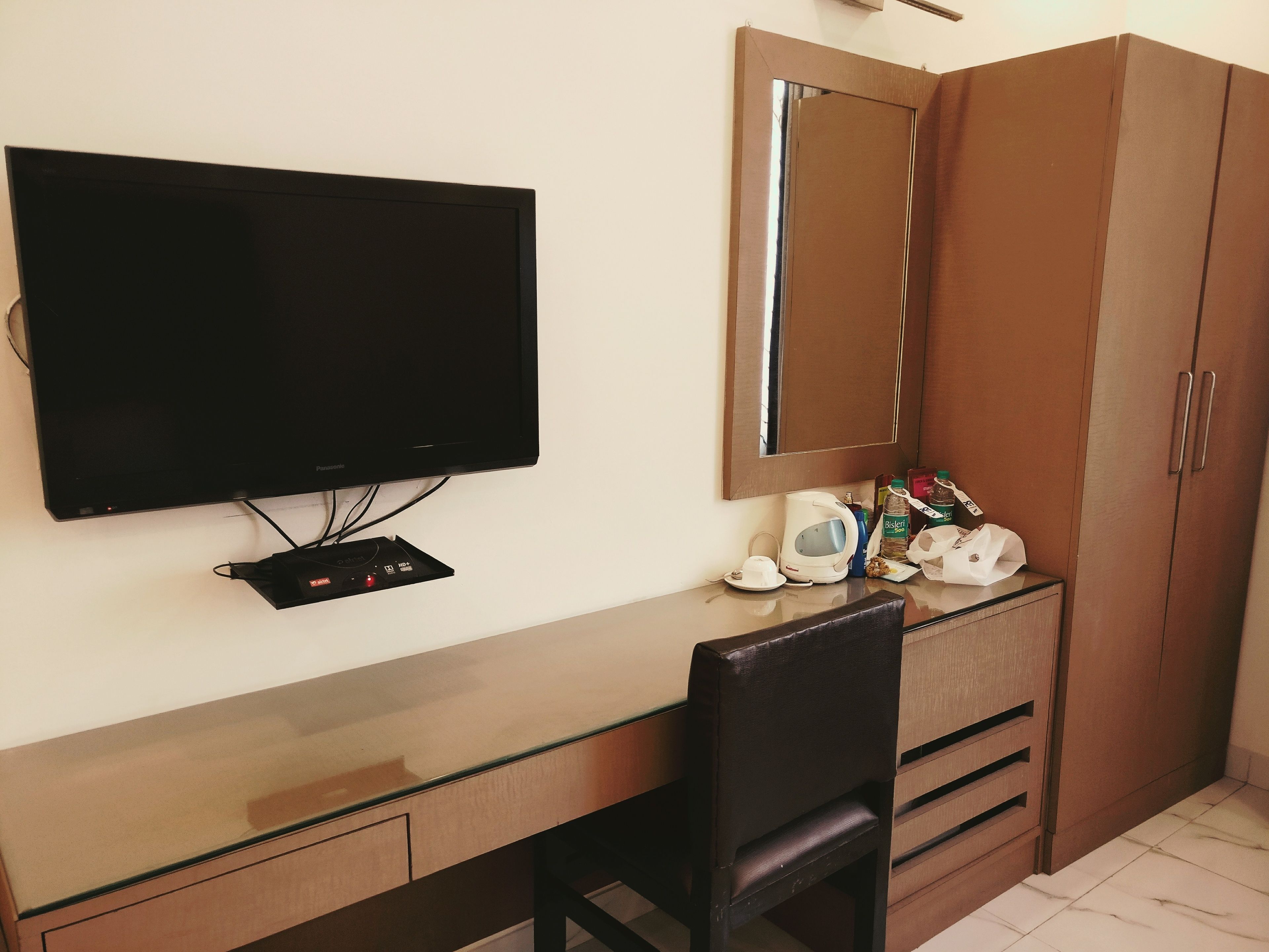 Una habitación de hotel con televisión de pantalla plana, cafetera, espejo y armario de madera.