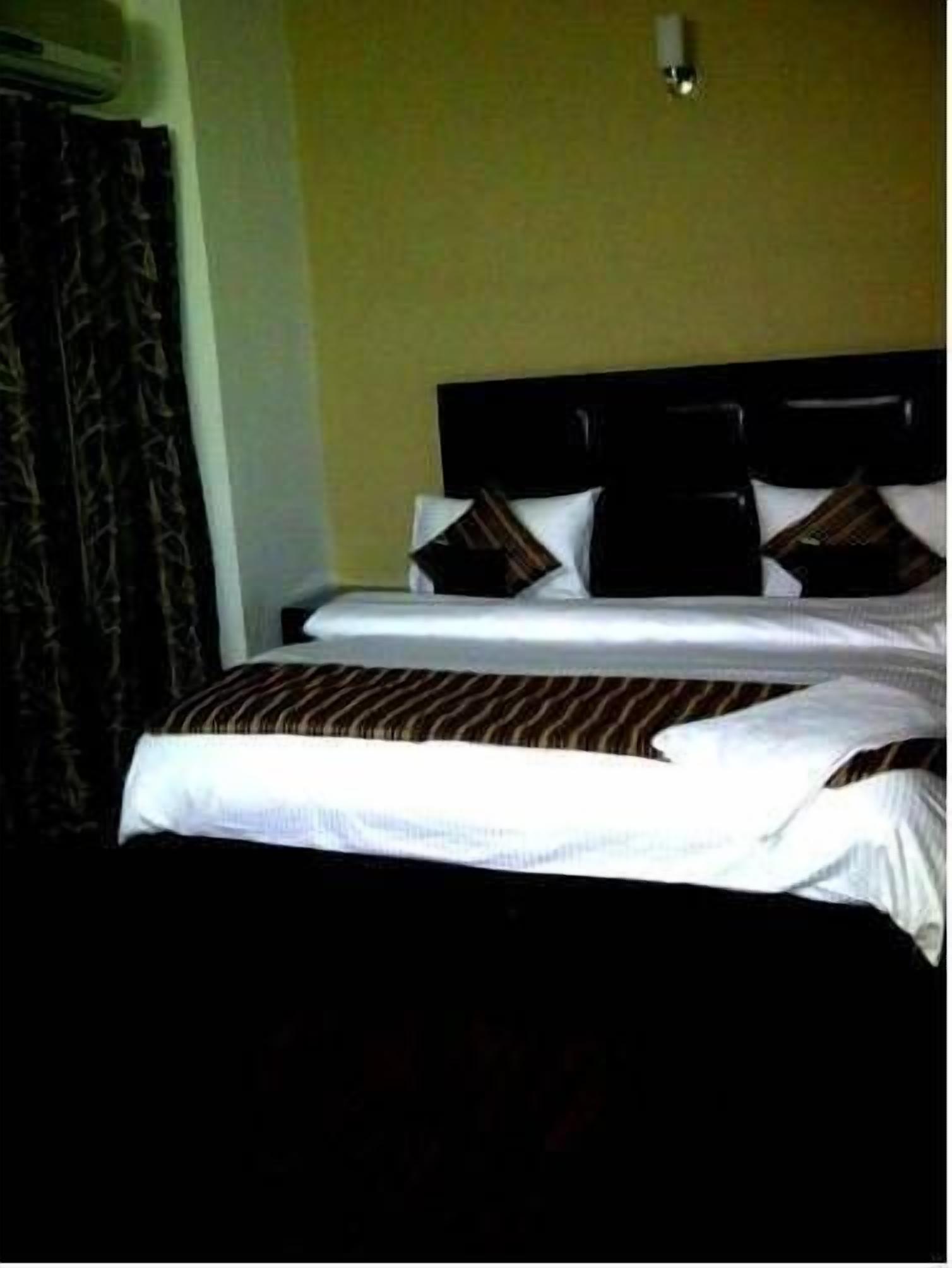 A hotel room with a bed, a headboard, and a wall-mounted light fixture.