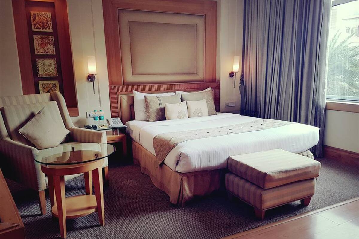 Een hotelkamer met een groot bed, een zithoek met een glazen tafeltje en een nachtkastje met een lamp.