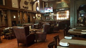 A restaurant with wooden floors, leather seating, a bar area, and a clock on the wall. - The Palms - Town & Country Club (Gurugram)