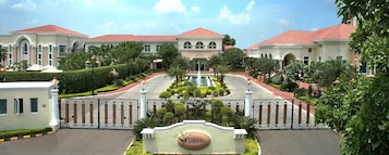 Een omheind landgoed met een centrale fontein, verzorgde tuinen en een bord waarop staat 'The Palms Town & Country Club'.