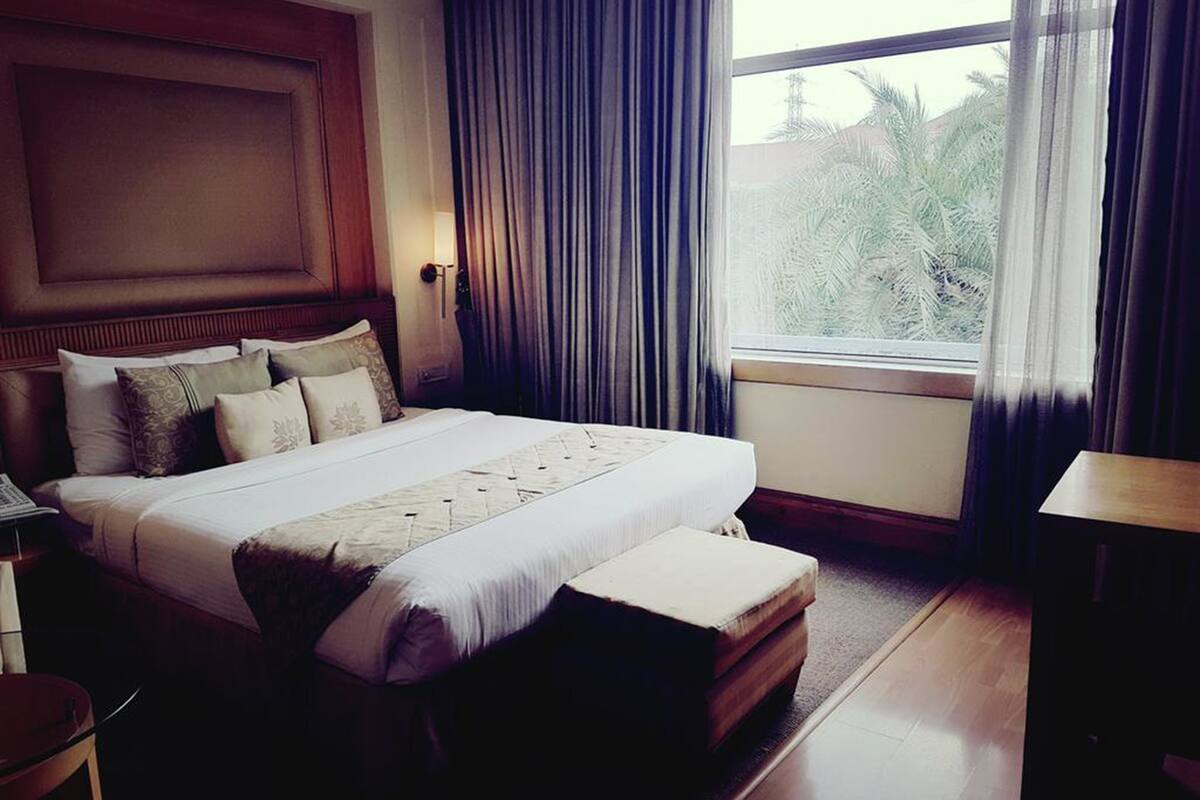 Een hotelkamer met een groot bed, een houten hoofdbord, een nachtkastje, een bureau en een raam met gordijnen.