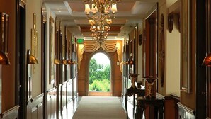 A long, elegant hallway with a grand chandelier, framed artwork on the walls, and a clear view to the outdoors. - The Palms - Town & Country Club (Gurugram)