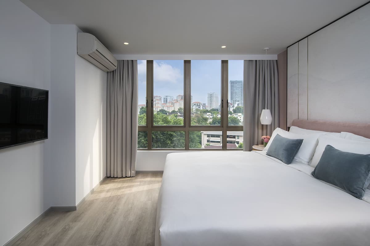 A hotel room with a large bed, a flat-screen TV mounted on the wall, a window with curtains, and a city view.
