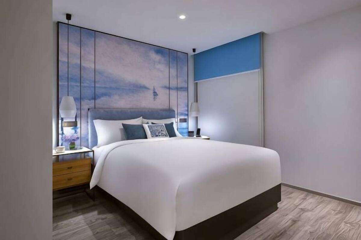 A modern bedroom with a large bed, bedside tables, and a wall-mounted artwork.