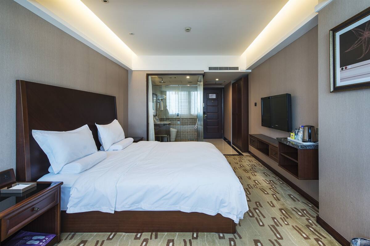 Habitación de hotel con una cama grande, mesitas de noche, televisión y baño a la vista a través de una puerta abierta.