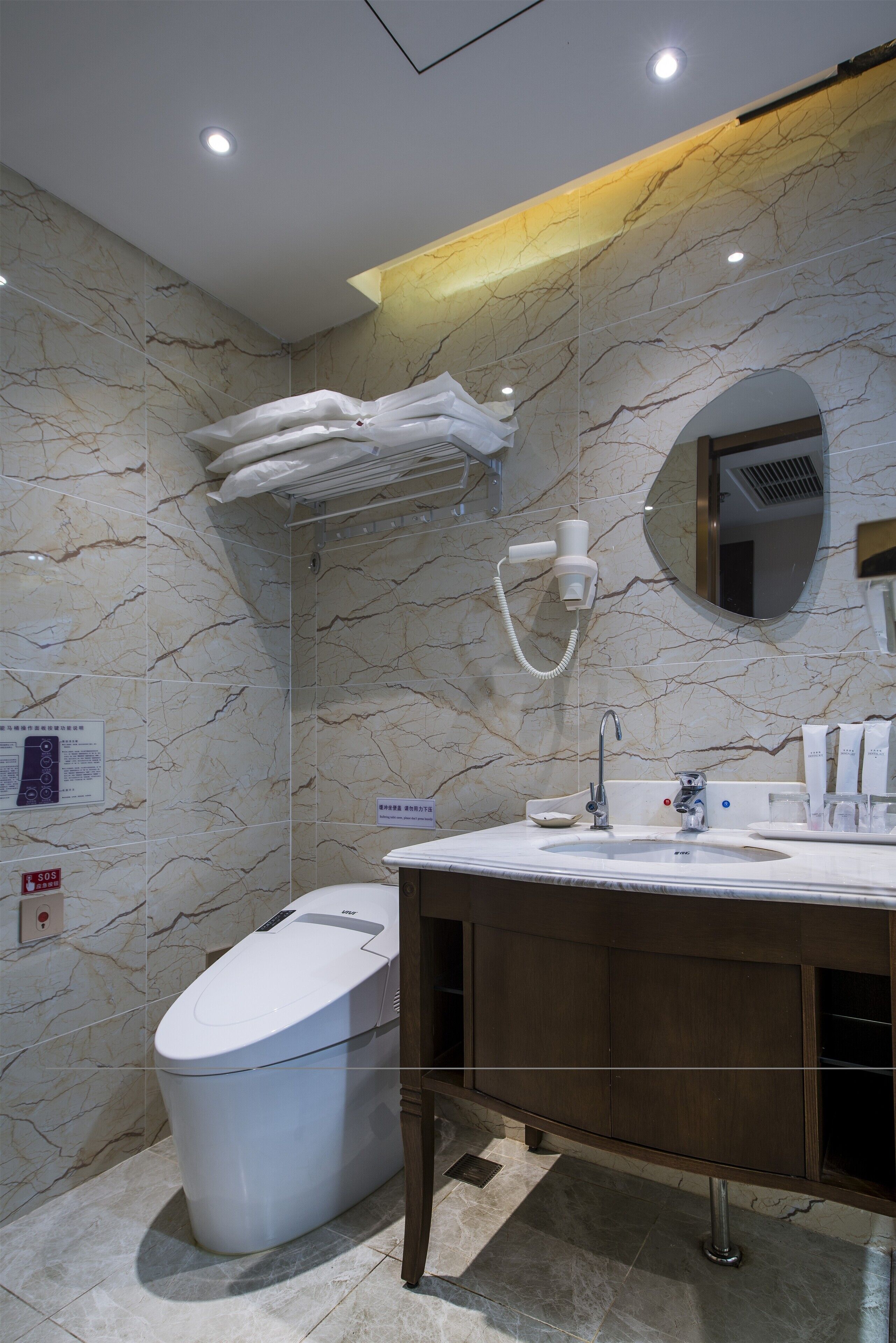 Une salle de bain moderne avec un mur en marbre, des toilettes, un lavabo avec un miroir et un porte-serviettes.
