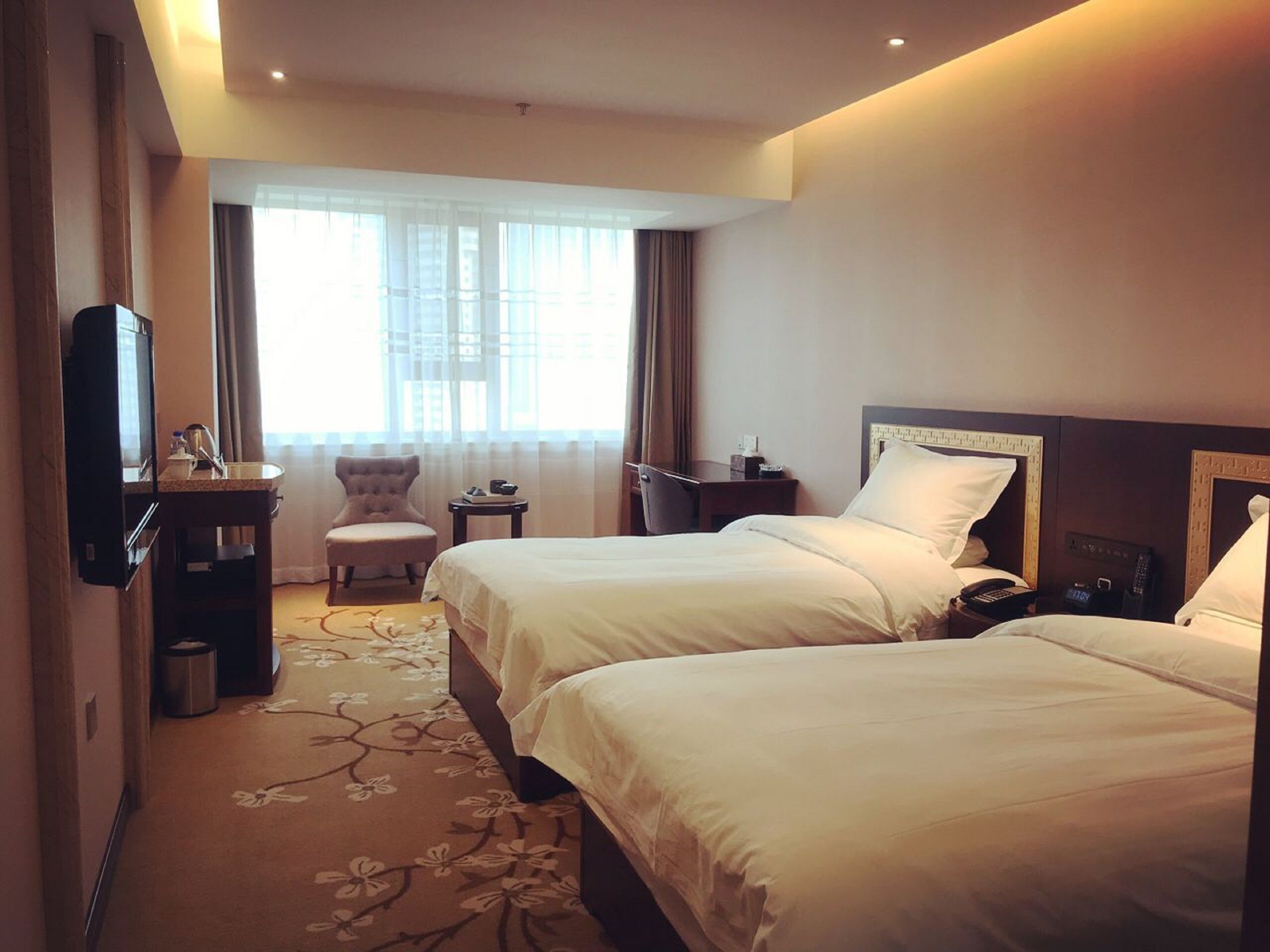 A hotel room with two beds, a desk, a chair, a TV, and a window with curtains.