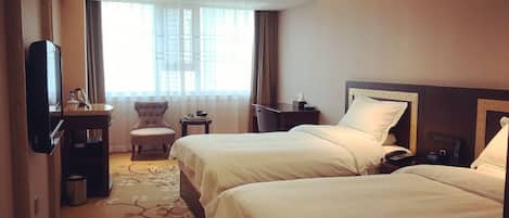A hotel room with two beds, a desk, a chair, a TV, and a window with curtains.